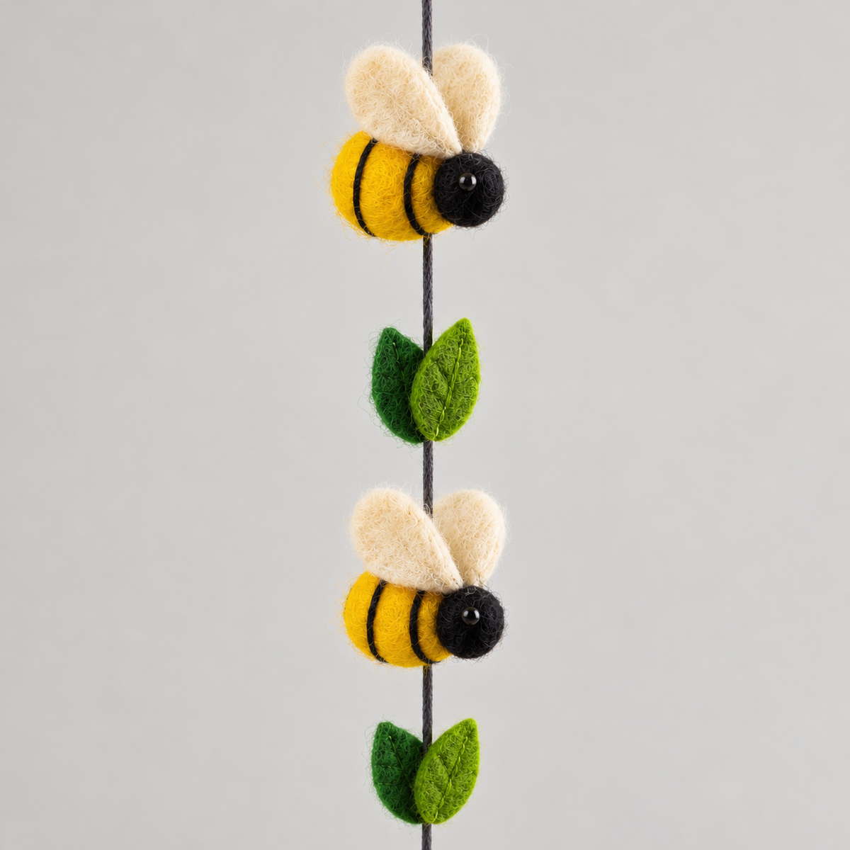 Detail of two yellow and black wool bees and green felt leaves