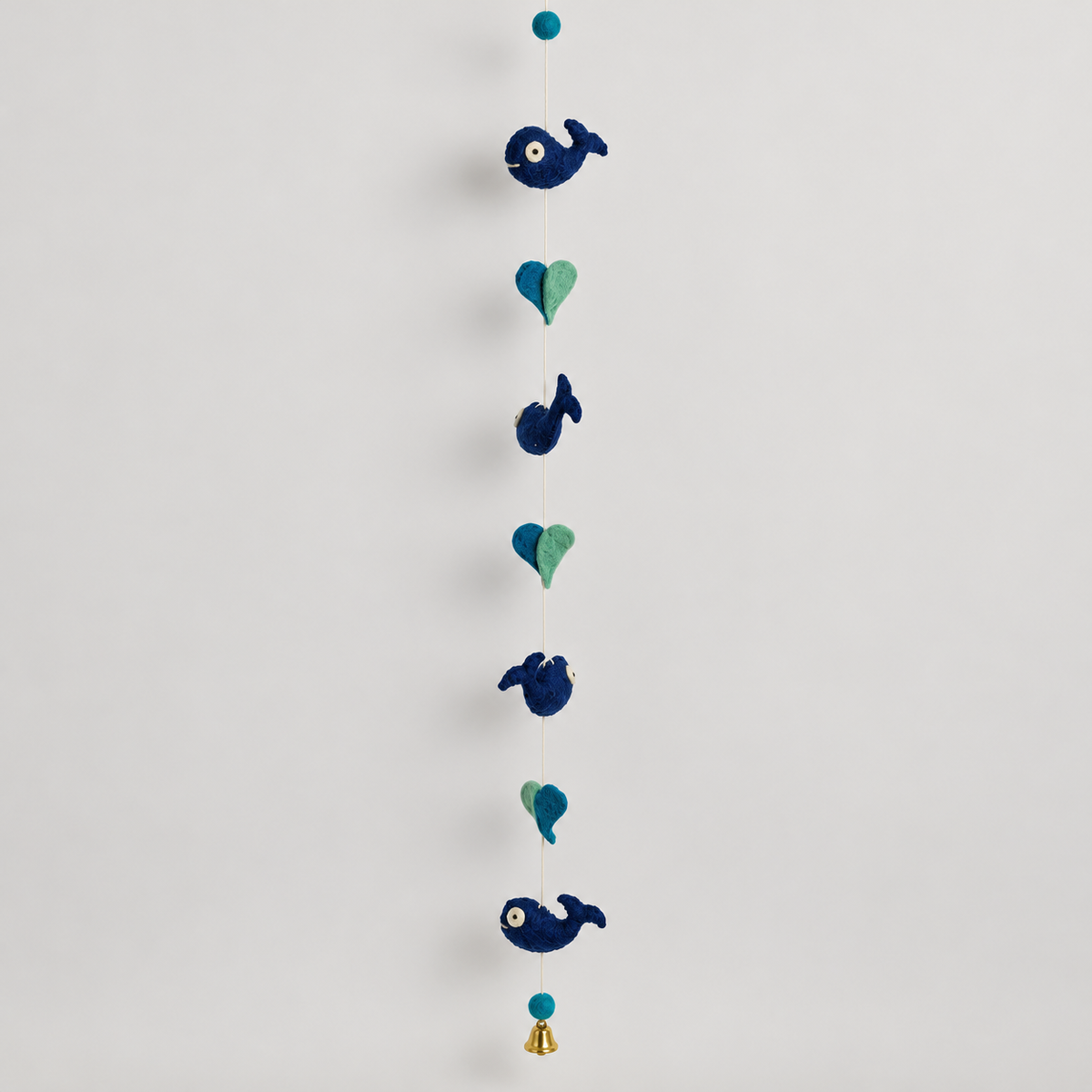Full handmade navy whale and teal heart wool garland with bell on warm gray