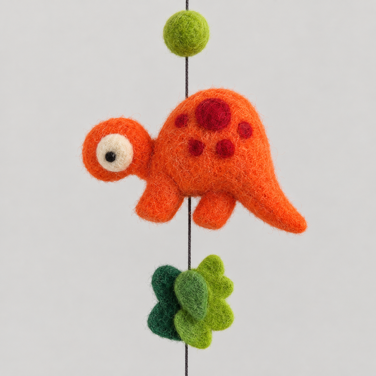 Orange wool dinosaur with red spots and green felt leaves close-up