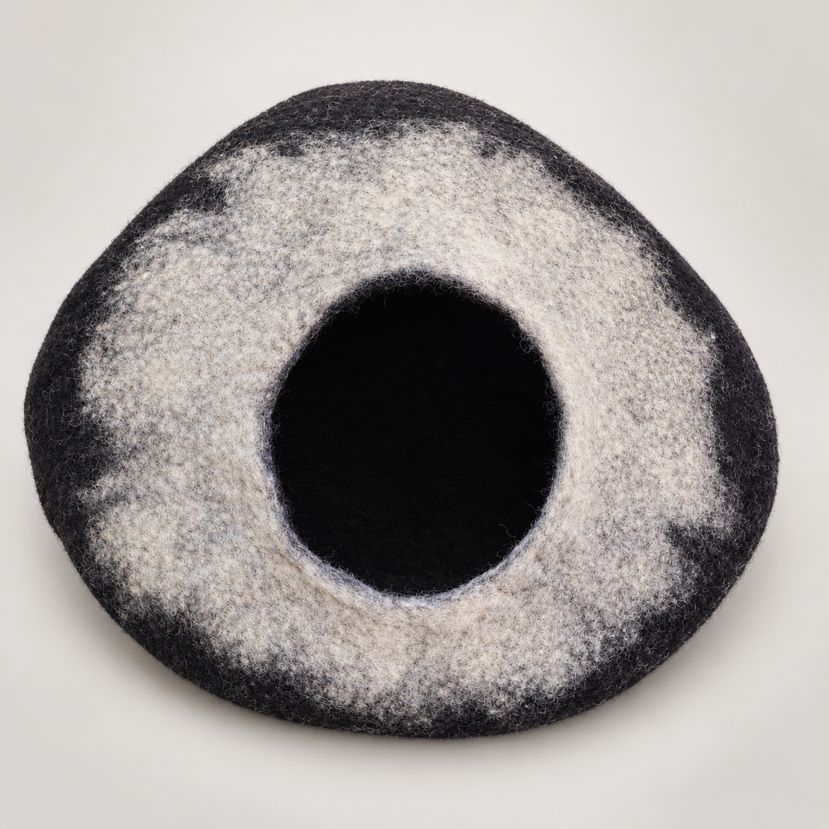 Charcoal and light-gray handmade wool cat cave on warm soft gray background
