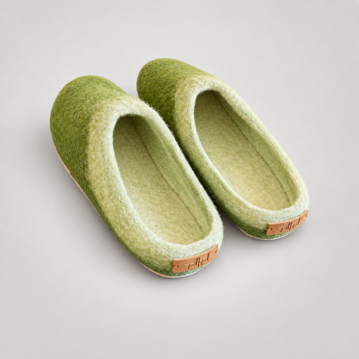 Green and cream wool felt slippers with clean empty interiors on warm gray