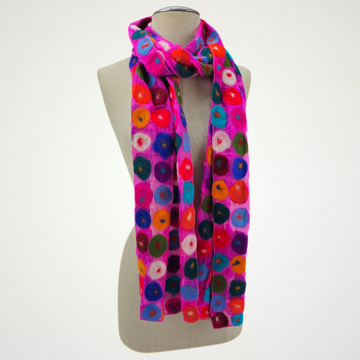 fuchsia scarf covered with multicolored circle motifs, looped around a mannequin's neck